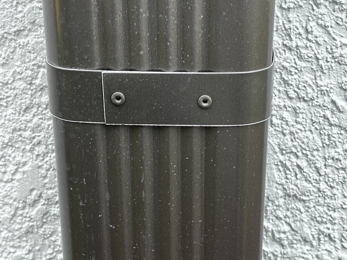 Bronze downspout, riveted band, against white stucco