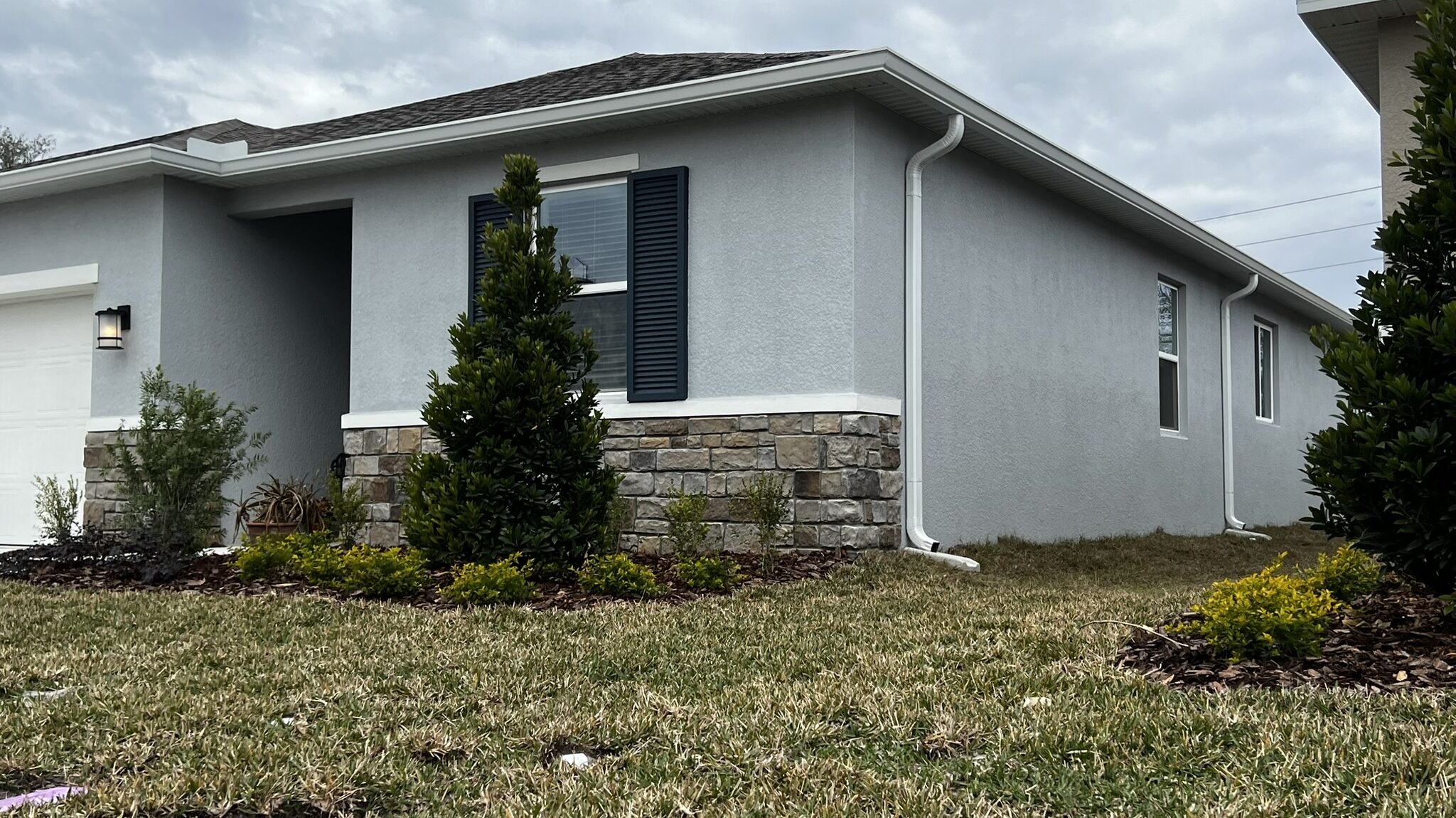 White downspout running down a stucco wall to a concrete splash block
